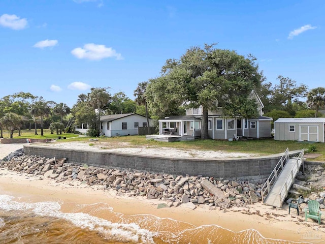 view of front of property with a storage unit, a view of the beach, an outbuilding, and a water view