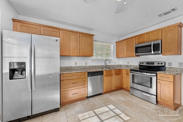 kitchen with sink, ceiling fan, light stone countertops, appliances with stainless steel finishes, and light tile patterned flooring