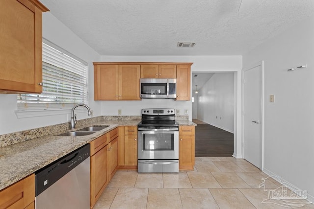 kitchen featuring light stone countertops, sink, stainless steel appliances, a textured ceiling, and light tile patterned flooring