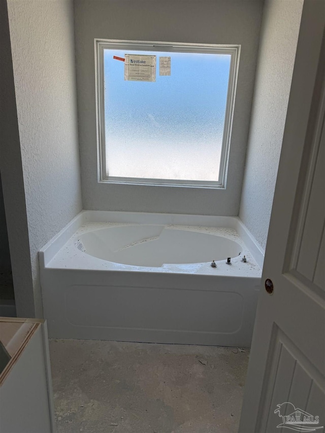 bathroom featuring a bath, plenty of natural light, and a textured wall