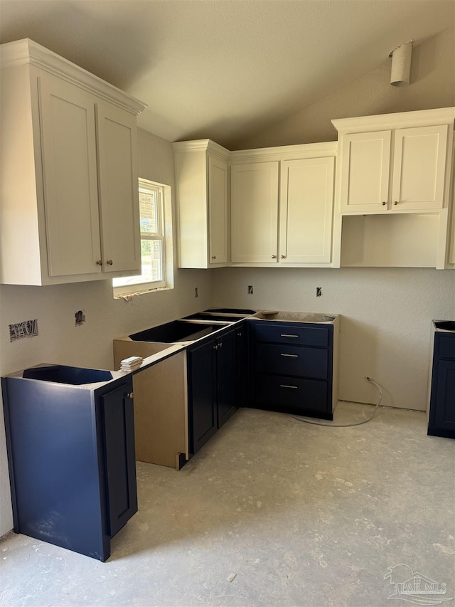 kitchen with vaulted ceiling, concrete floors, and white cabinetry