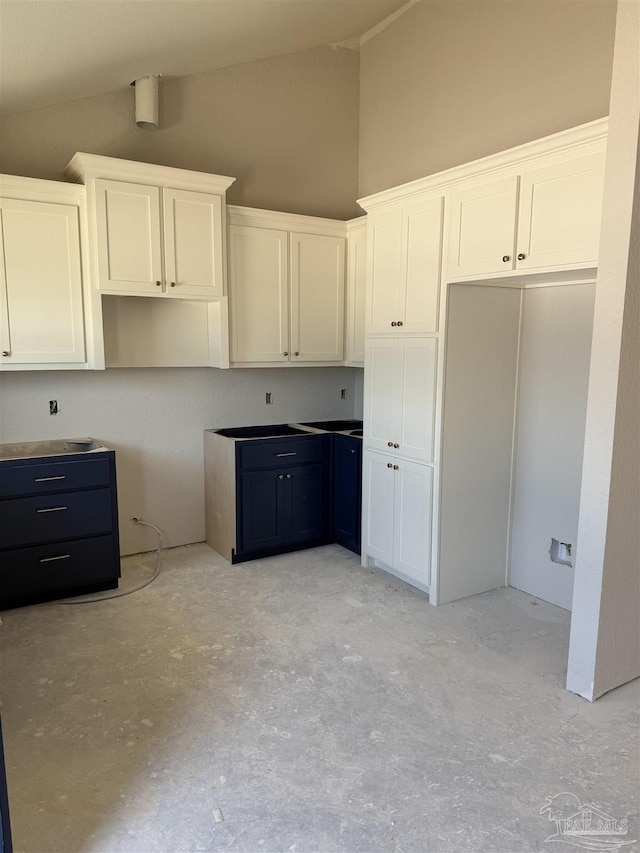 kitchen featuring vaulted ceiling, concrete flooring, and white cabinetry