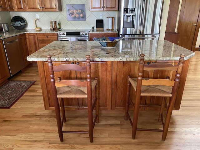 kitchen with decorative backsplash, stainless steel appliances, light stone counters, and light hardwood / wood-style floors