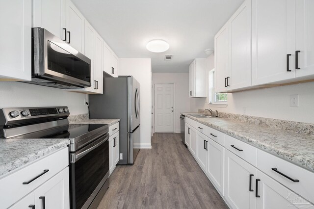 kitchen with white cabinets, appliances with stainless steel finishes, light stone countertops, light hardwood / wood-style floors, and sink