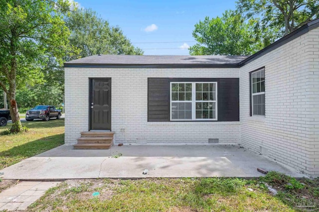doorway to property with a yard, a patio area, brick siding, and crawl space