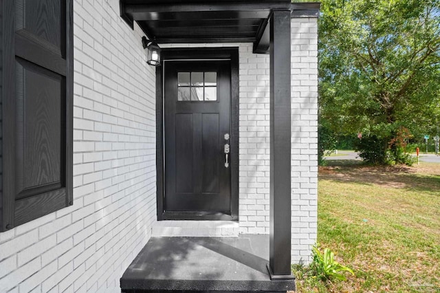 view of exterior entry with a lawn and brick siding
