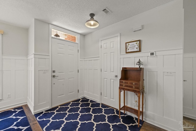 foyer entrance featuring wainscoting, visible vents, a textured ceiling, and dark wood-style flooring