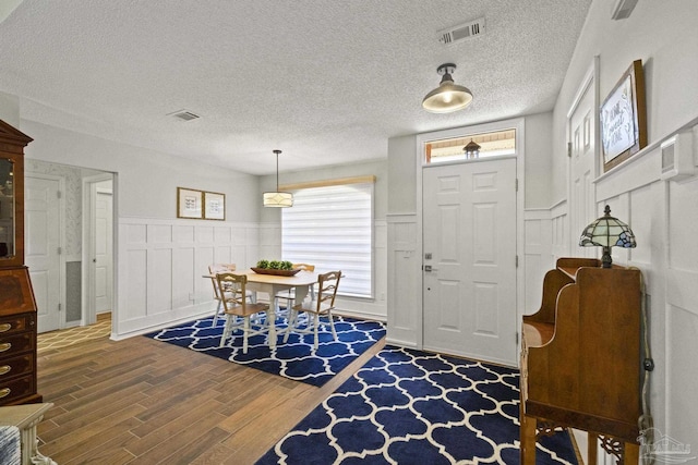 entrance foyer with a textured ceiling, visible vents, wood finished floors, and wainscoting