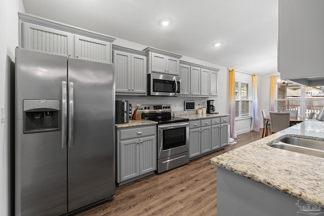 kitchen with light stone countertops, appliances with stainless steel finishes, dark hardwood / wood-style flooring, sink, and gray cabinets