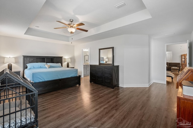 bedroom featuring connected bathroom, a raised ceiling, ceiling fan, and dark wood-type flooring