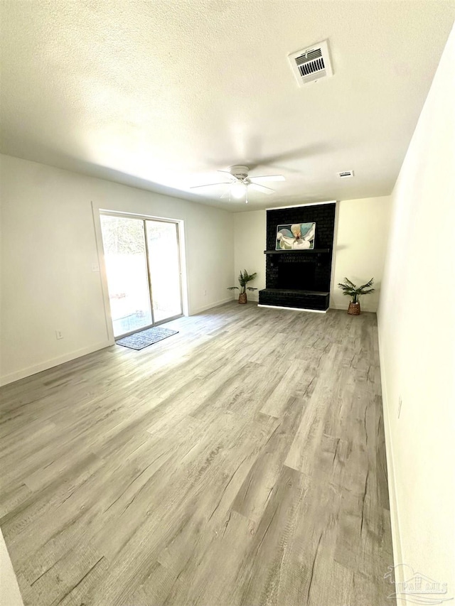 unfurnished living room with a fireplace, ceiling fan, light hardwood / wood-style flooring, and a textured ceiling