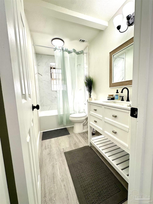 full bathroom featuring shower / bath combination with curtain, vanity, a textured ceiling, hardwood / wood-style floors, and toilet