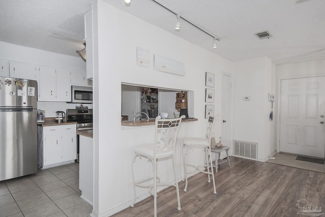 kitchen with appliances with stainless steel finishes, white cabinets, a textured ceiling, and light hardwood / wood-style floors