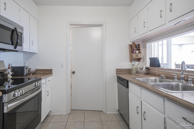 kitchen with appliances with stainless steel finishes, sink, light tile patterned floors, and white cabinets