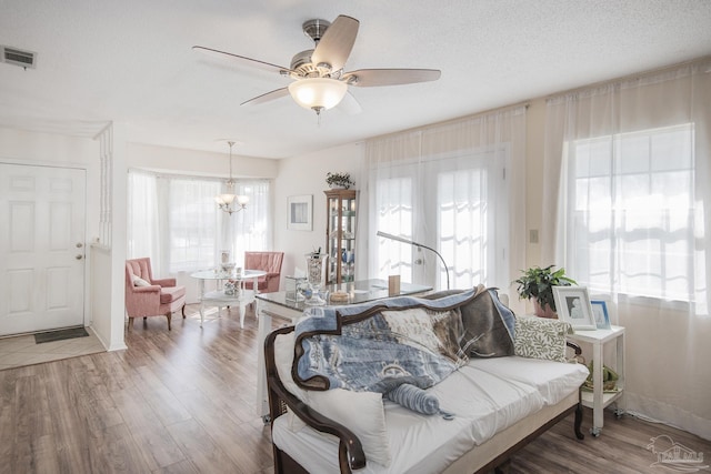 living room featuring wood-type flooring, ceiling fan with notable chandelier, and a textured ceiling