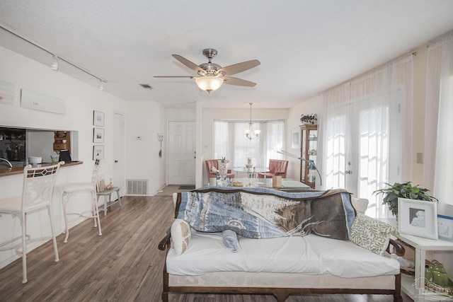 living room with ceiling fan with notable chandelier, rail lighting, hardwood / wood-style floors, and a textured ceiling