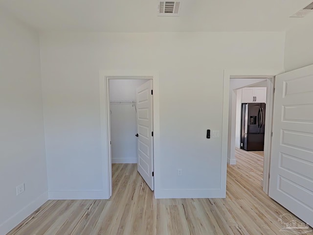 unfurnished bedroom with light wood finished floors, baseboards, visible vents, and stainless steel fridge with ice dispenser