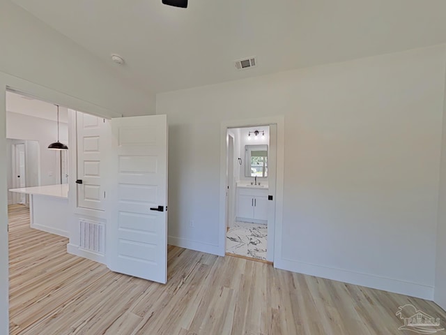 spare room featuring light wood-type flooring, visible vents, a sink, and baseboards