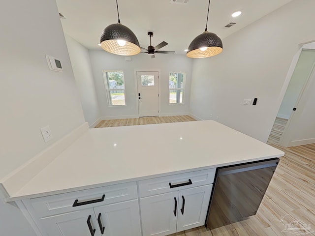 kitchen with white cabinets, light countertops, stainless steel dishwasher, light wood finished floors, and decorative light fixtures