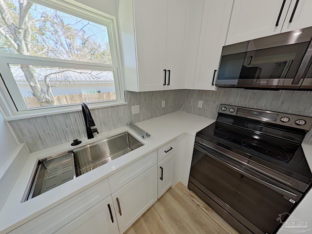 kitchen with black range with electric cooktop, white cabinetry, light countertops, backsplash, and stainless steel microwave