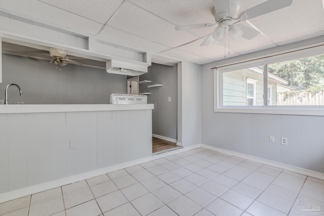 interior space with baseboards, light tile patterned flooring, a drop ceiling, ceiling fan, and a sink