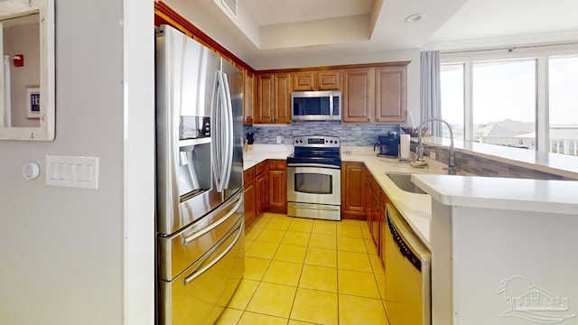 kitchen featuring a raised ceiling, light countertops, backsplash, appliances with stainless steel finishes, and a sink