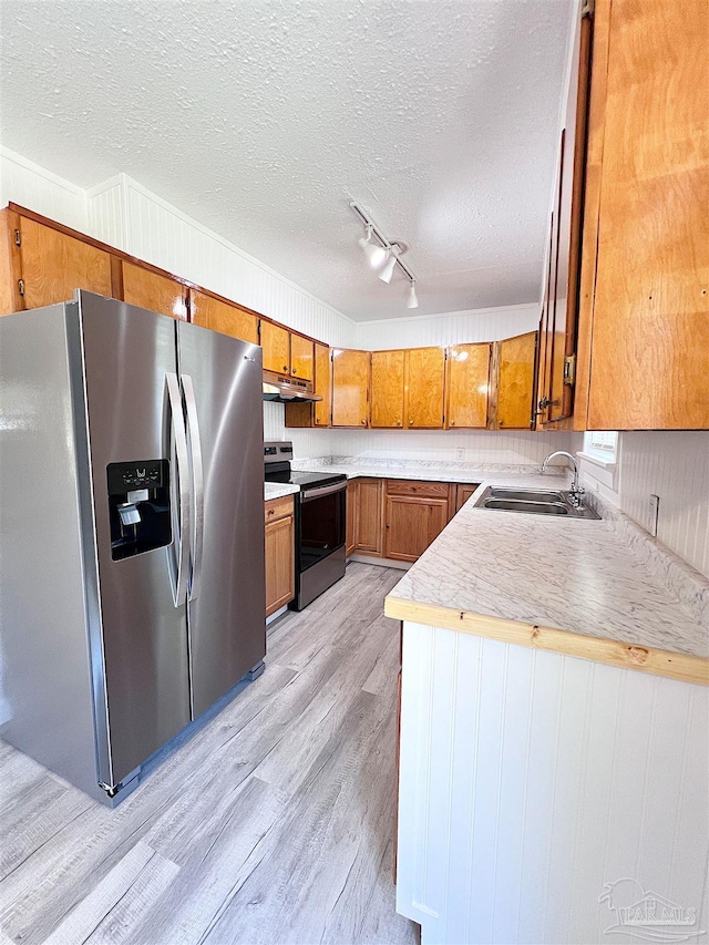 kitchen with light wood-style flooring, appliances with stainless steel finishes, brown cabinets, under cabinet range hood, and a sink