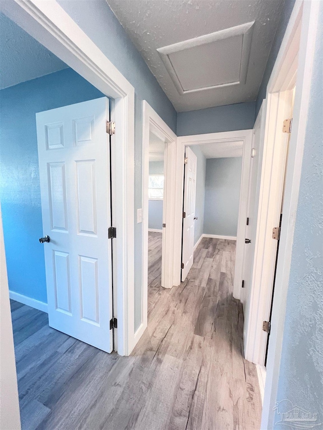 corridor featuring wood finished floors, attic access, and baseboards