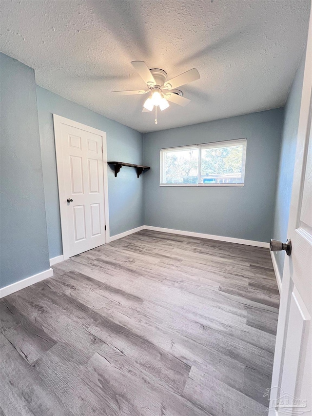 unfurnished bedroom with ceiling fan, a textured ceiling, baseboards, and wood finished floors