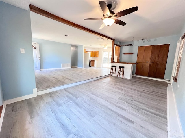 unfurnished living room featuring wood finished floors, visible vents, a ceiling fan, baseboards, and beam ceiling