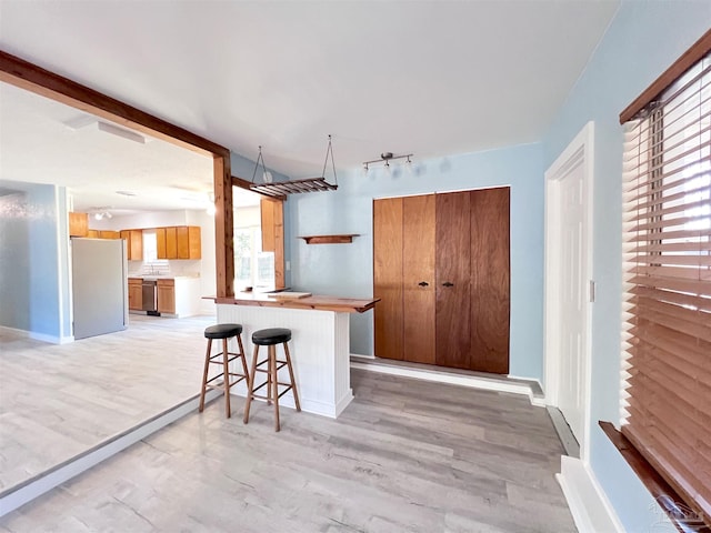 kitchen with a breakfast bar, light wood-style flooring, brown cabinetry, freestanding refrigerator, and a peninsula