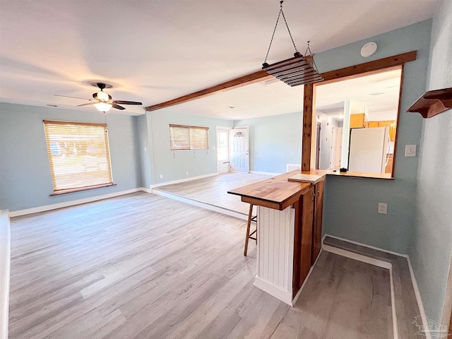 interior space with beam ceiling, ceiling fan, baseboards, and wood finished floors