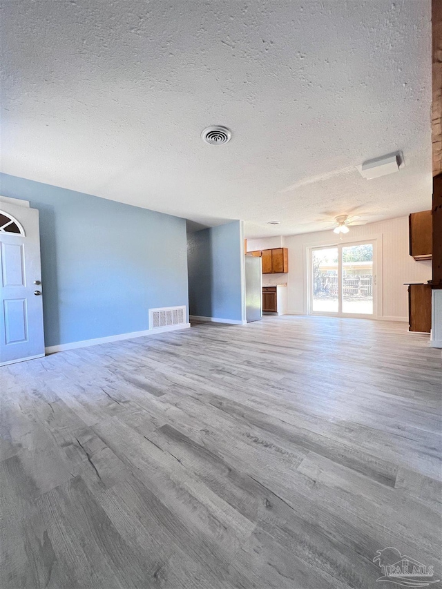 unfurnished living room featuring a textured ceiling, light wood finished floors, visible vents, and baseboards