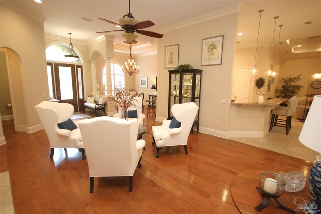 living room with arched walkways, decorative columns, baseboards, light wood-style floors, and ceiling fan with notable chandelier