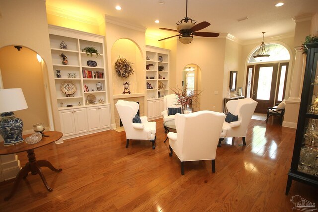 living area with recessed lighting, wood finished floors, a ceiling fan, arched walkways, and crown molding
