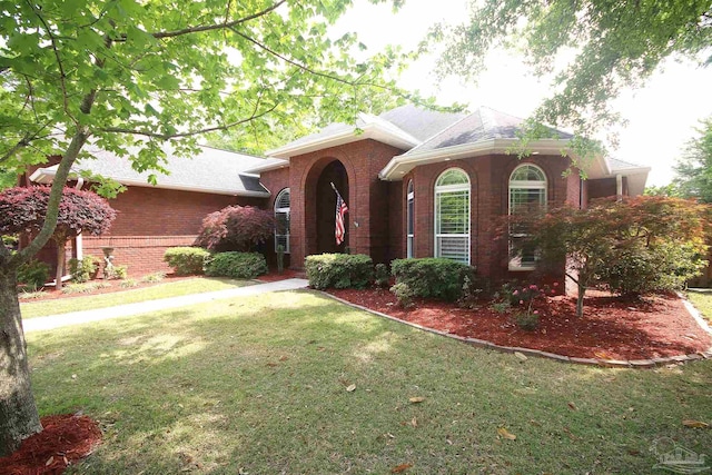 view of front of house with a shingled roof, a front lawn, and brick siding