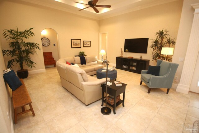 living room featuring a ceiling fan, light tile patterned floors, arched walkways, baseboards, and ornamental molding