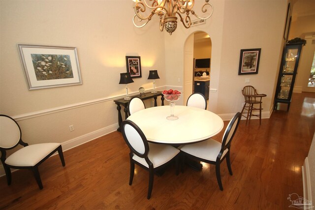 dining space featuring arched walkways, a chandelier, wood finished floors, and baseboards