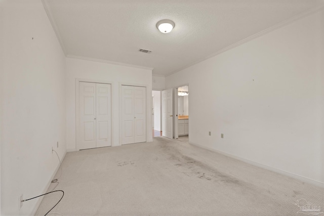 unfurnished bedroom with a textured ceiling, multiple closets, light carpet, connected bathroom, and ornamental molding