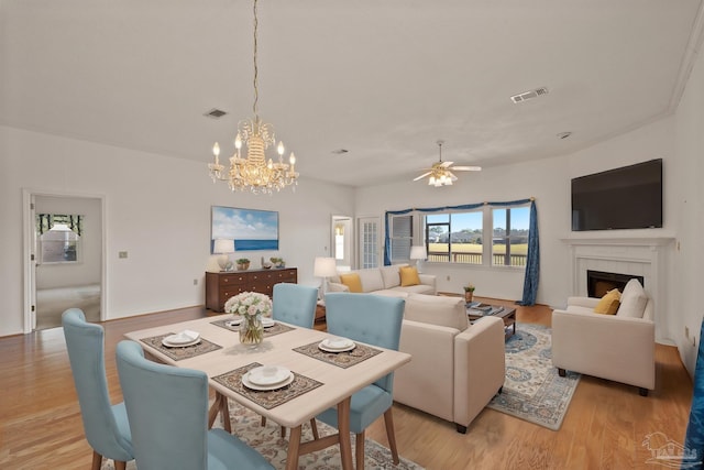 dining space with ceiling fan with notable chandelier, a tiled fireplace, and light hardwood / wood-style flooring