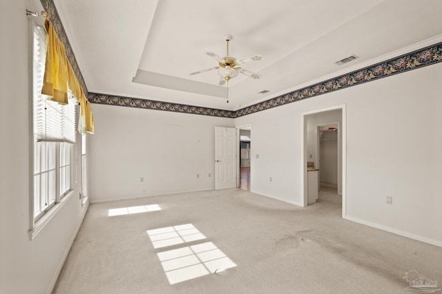 unfurnished bedroom with a spacious closet, a closet, light colored carpet, a tray ceiling, and ceiling fan