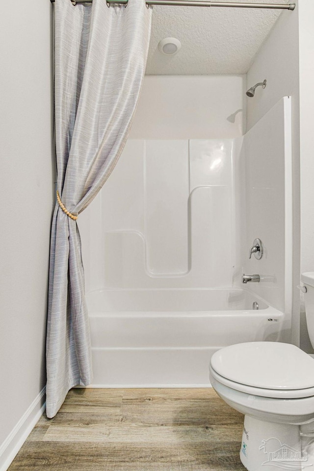 bathroom with toilet, wood-type flooring, a textured ceiling, and shower / tub combo