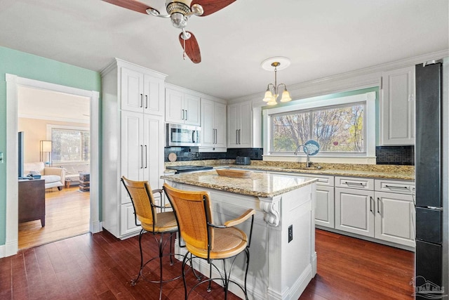 kitchen featuring decorative light fixtures, a center island, sink, light stone countertops, and white cabinets