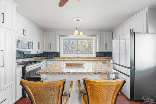 kitchen featuring appliances with stainless steel finishes, light stone countertops, a kitchen island, pendant lighting, and white cabinets