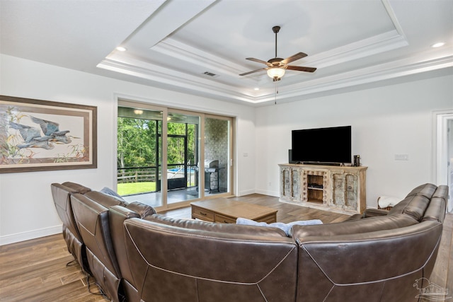 living room featuring a raised ceiling, ceiling fan, and light hardwood / wood-style floors