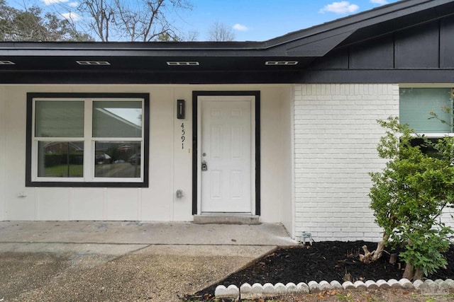 property entrance featuring board and batten siding and brick siding