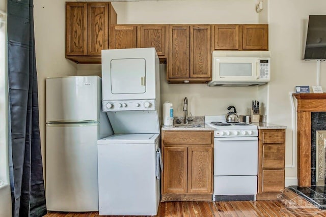 kitchen with white appliances, hardwood / wood-style flooring, sink, and stacked washer and dryer