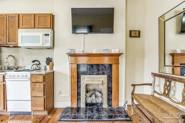 kitchen with a fireplace, white appliances, hardwood / wood-style floors, and sink