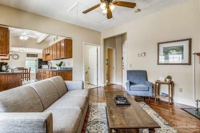 living room with ceiling fan, sink, beamed ceiling, and hardwood / wood-style flooring