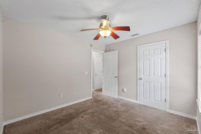 unfurnished bedroom featuring ceiling fan, a textured ceiling, visible vents, baseboards, and carpet flooring